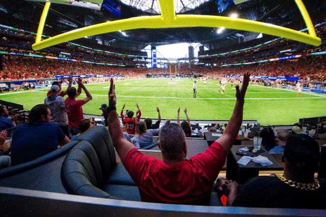 Fans signaling touch down gesture as they watch the football field infront of them in VIP booths